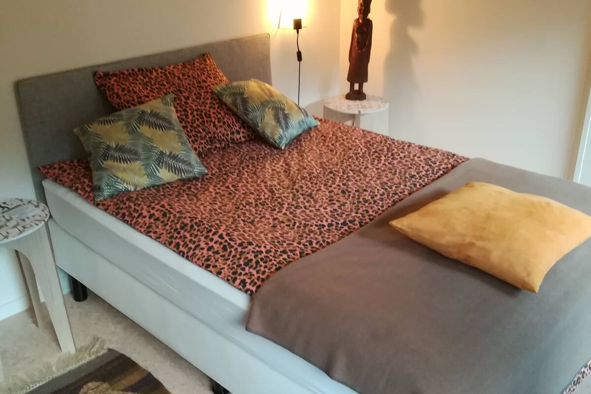 A bedroom with a bed, pillows, a nightstand, a statue, and framed pictures on the wall.