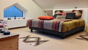 A bedroom with a sloped ceiling, a bed with multiple pillows, a window, and a radiator. - B&B Golf Schilde (Schilde)