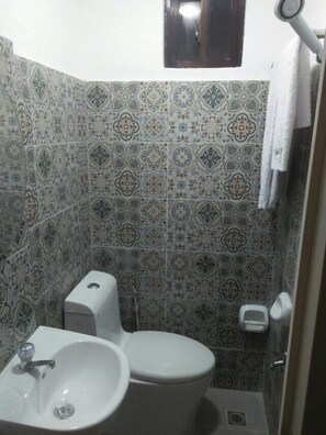 A bathroom with a white sink, toilet, and shower. The walls are tiled with a patterned design.