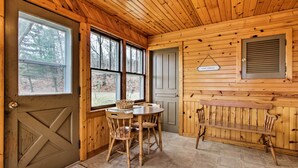 A wooden interior with a dining table and chairs, a bench, and a door with a sign. - Wisconsin River Valley Farmhouse: Fire Pit & View (Portage)