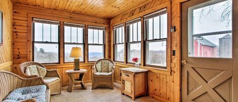 A cozy cabin interior with wooden walls, large windows, wicker furniture, and a door with a cross design.