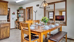 A dining area with a wooden table set for four, surrounded by wooden chairs with leather cushions. A large mirror reflects the room, and a hanging light fixture is visible above the table. - Wisconsin River Valley Farmhouse: Fire Pit & View (Portage)