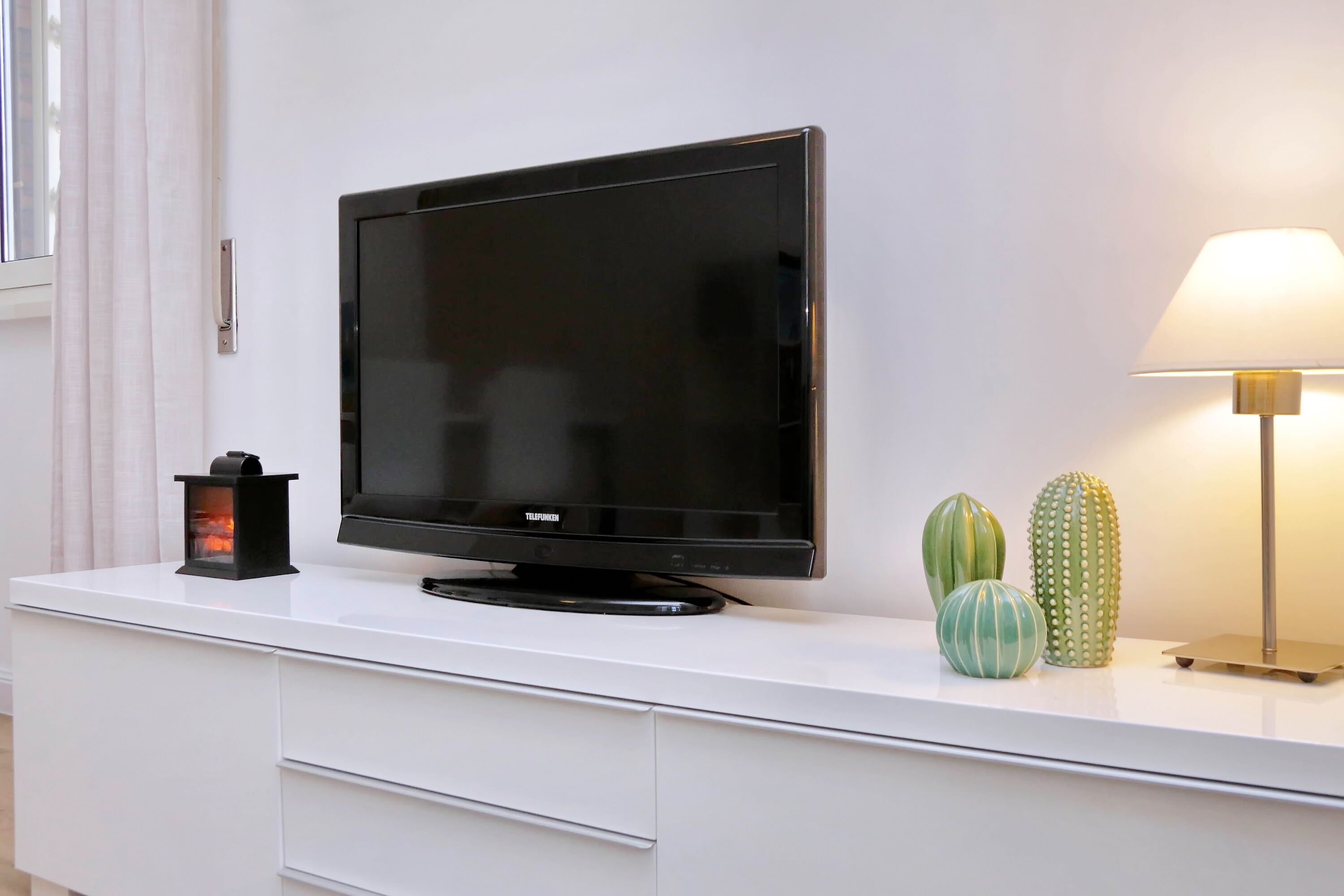 A flat-screen TV on a white cabinet, a lamp, and three cacti.