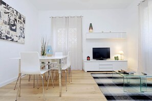 A modern living room with a dining area, a flat-screen TV, and a glass coffee table. - Magliana Apartment (Rome)