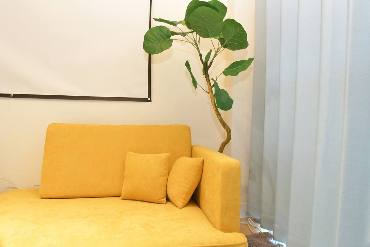 A yellow sofa with a cushion, a wall-mounted picture frame, and a potted plant.