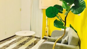Een kamer met een gestreept vloerkleed, een ronde witte tafel met een buisframe, een grijze bank en een grote groene plant.