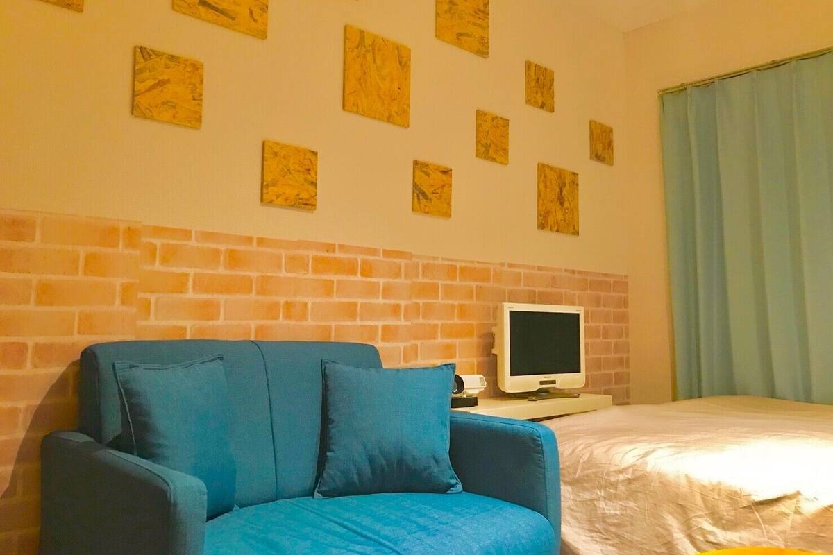 A hotel room with a brick wall, a blue sofa, a bed, a flat-screen TV, and a window with curtains.