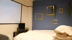 Een slaapkamer met een bed, een bureau met een laptop en een scherm voor een projector.
