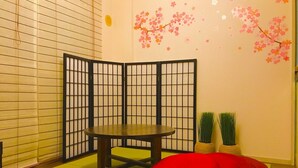 Een kamer met een tatami vloer, een lage tafel, een rode relaxfauteuil en een shoji schuifwand.