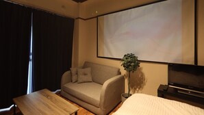 Een hotelkamer met een bank, een houten tafel, een televisie en een projectiescherm.