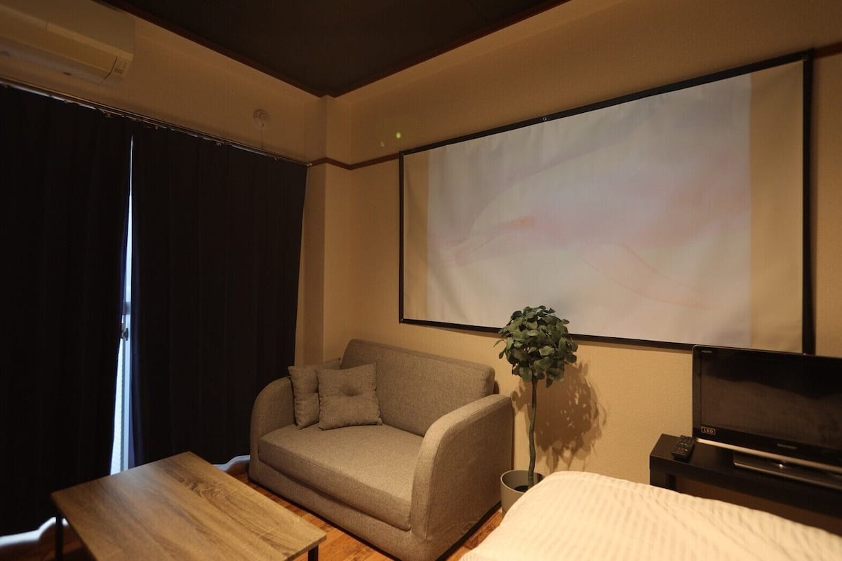 A hotel room with a sofa, a wooden table, a TV, and a projector screen.