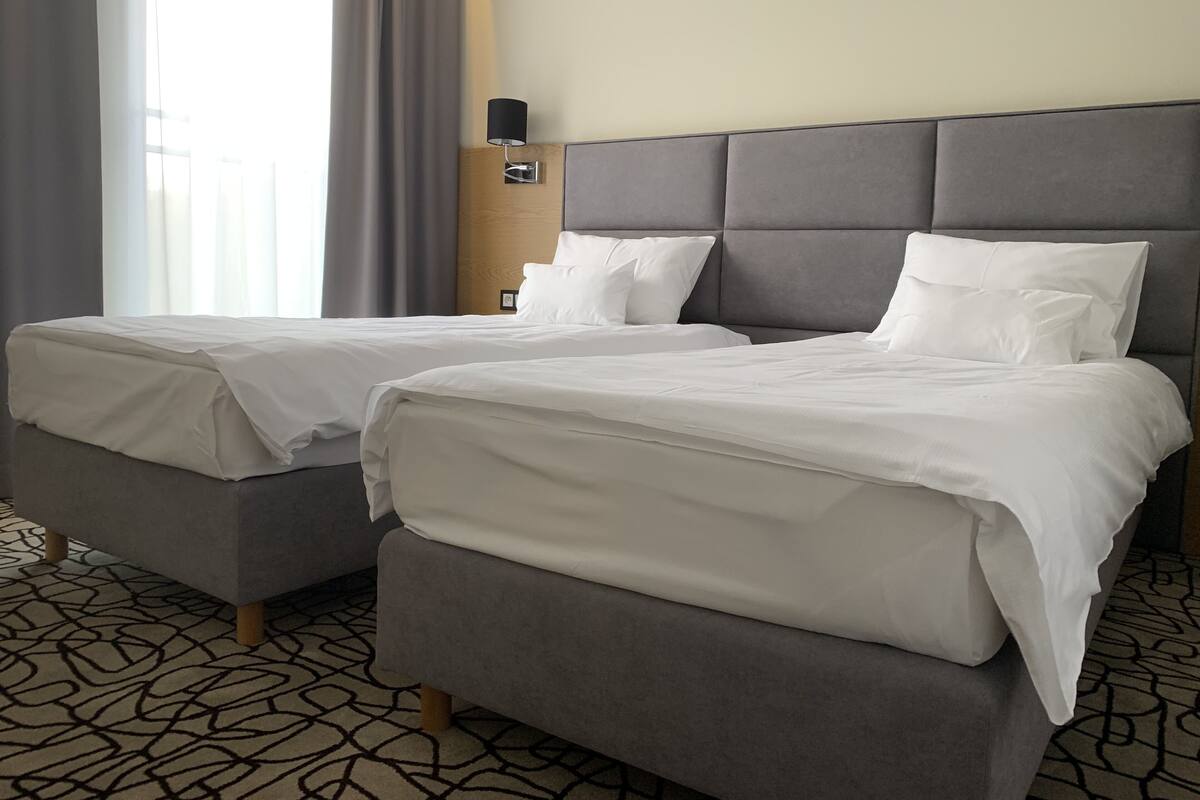 A hotel room with two beds, a nightstand, a lamp, and a patterned carpet.