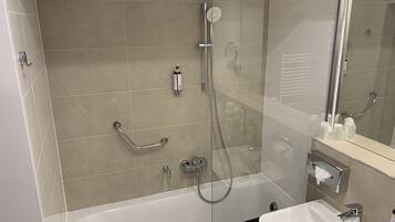 Een moderne badkamer met een douchecabine van glas, een witte badkuip en een wastafel met een spiegel erboven.