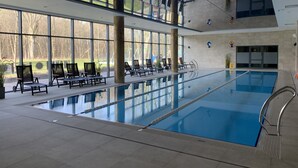 En inomhuspool med väggar av genomskinligt glas, solstolar och utsikt över omgivningen.