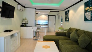 A modern living room with a green sofa, a white coffee table, and a TV mounted on the wall. - Sleek 1 bed Condo Jomtien (Pattaya)
