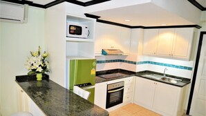 A compact kitchen with white cabinets, a black countertop, a microwave, a stove, and a sink. - Sleek 1 bed Condo Jomtien (Pattaya)