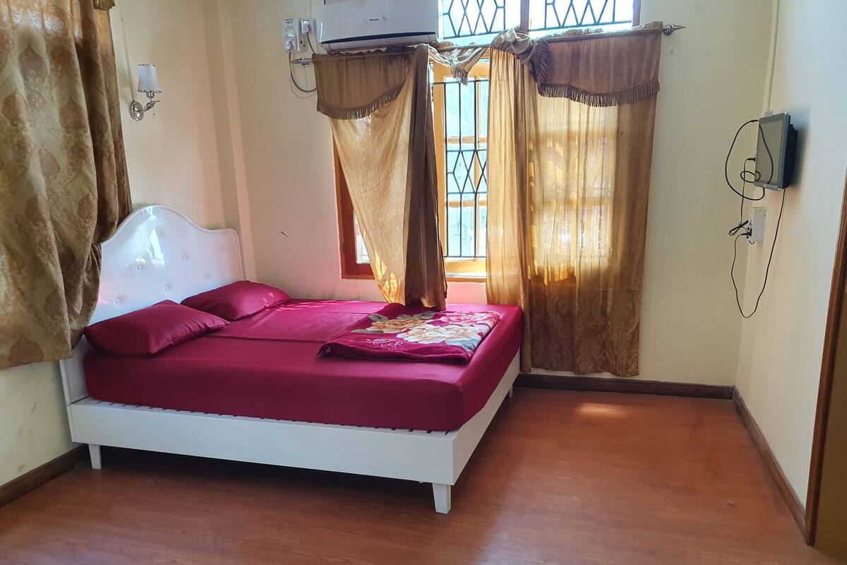 Un dormitorio con cama blanca, ropa de cama roja y cortinas marrones.