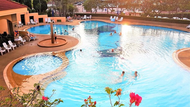 Una gran piscina cubierta con múltiples carriles, rodeada de sillones de descanso y una pequeña zona ajardinada.
