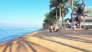 Una playa con palmeras y un edificio al fondo.