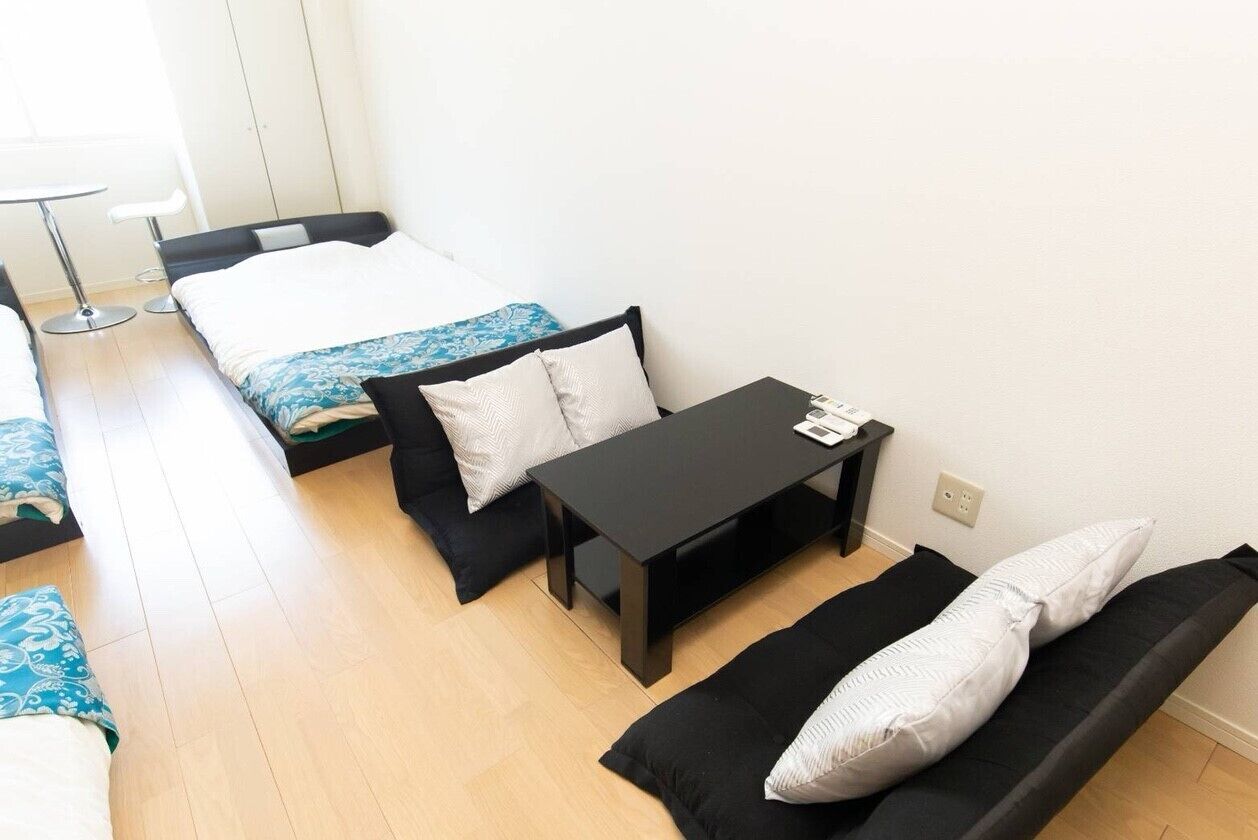 A compact hotel room with a bed, a small table, a sofa, and a chair.