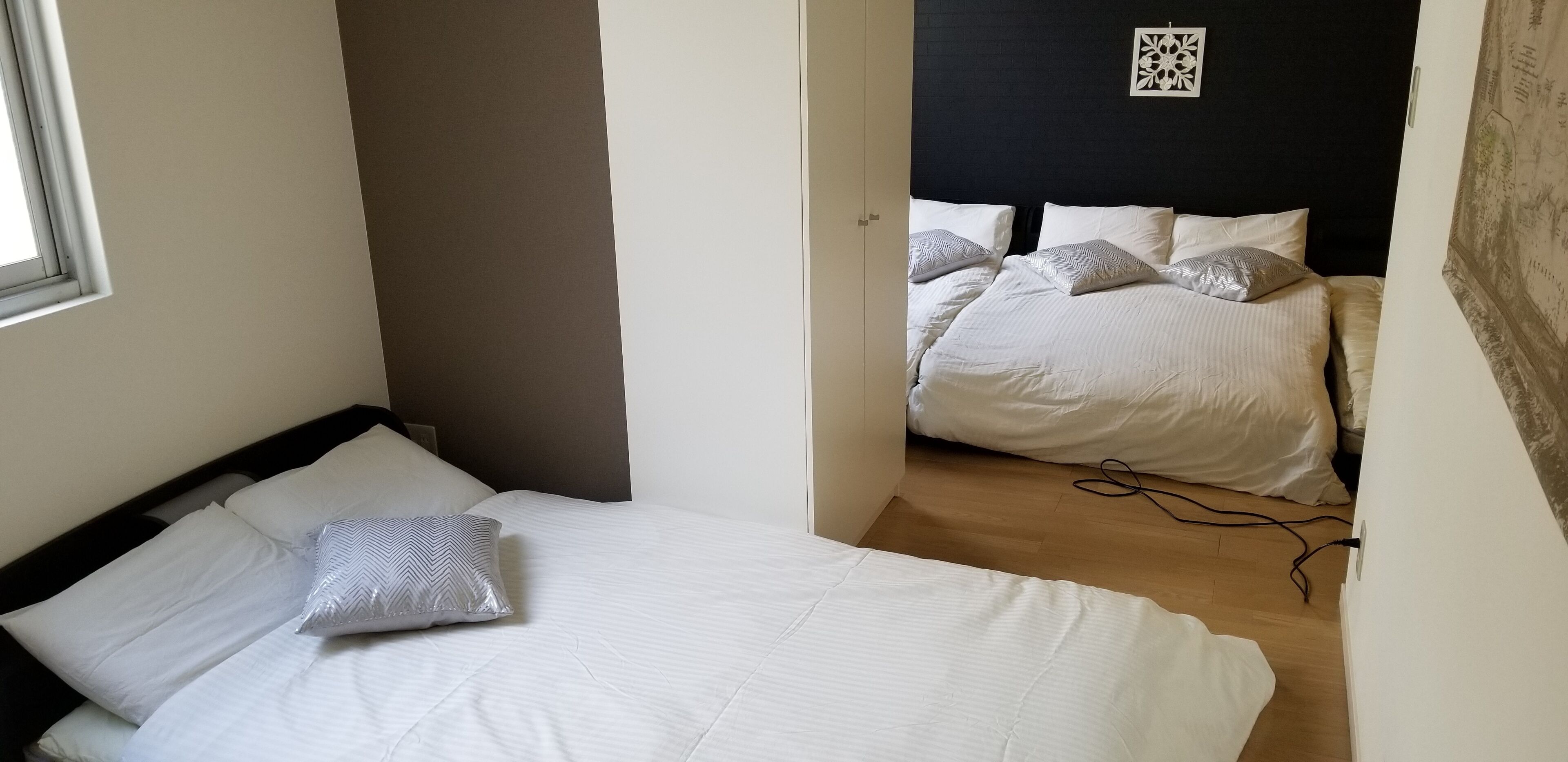 Un dormitori amb un llit individual, una finestra i una porta que dona a una altra habitació amb un llit més gran.
