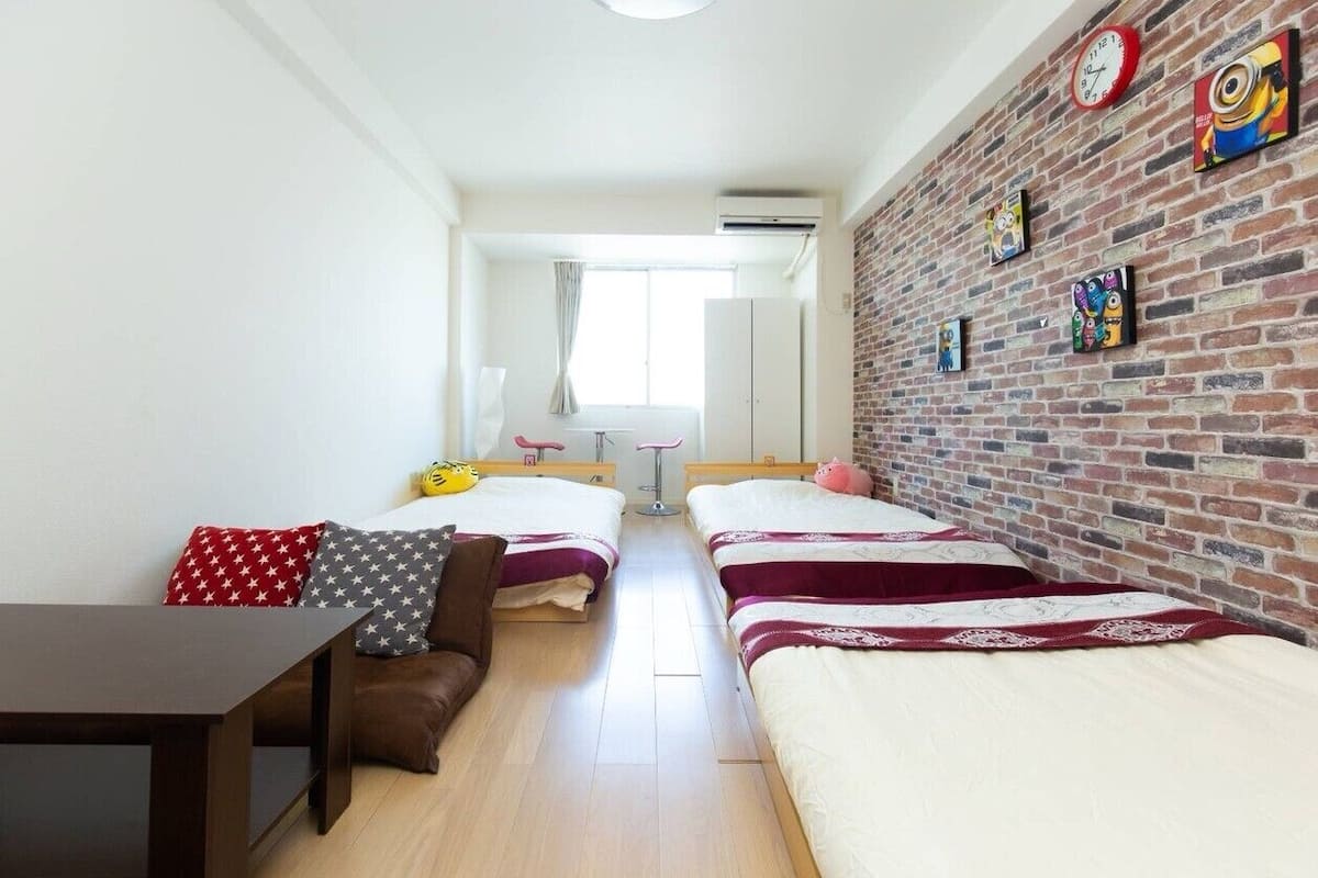 Una habitación con dos camas, una mesita pequeña, un sofá y una pared de ladrillo decorada con relojes y obras de arte.