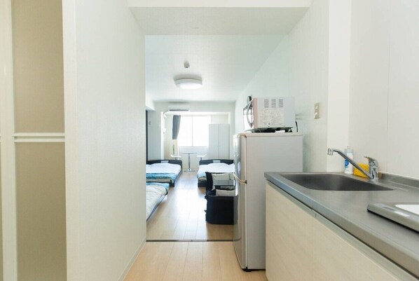 A narrow hallway leading to a bedroom with a bed, a small table, and a window.