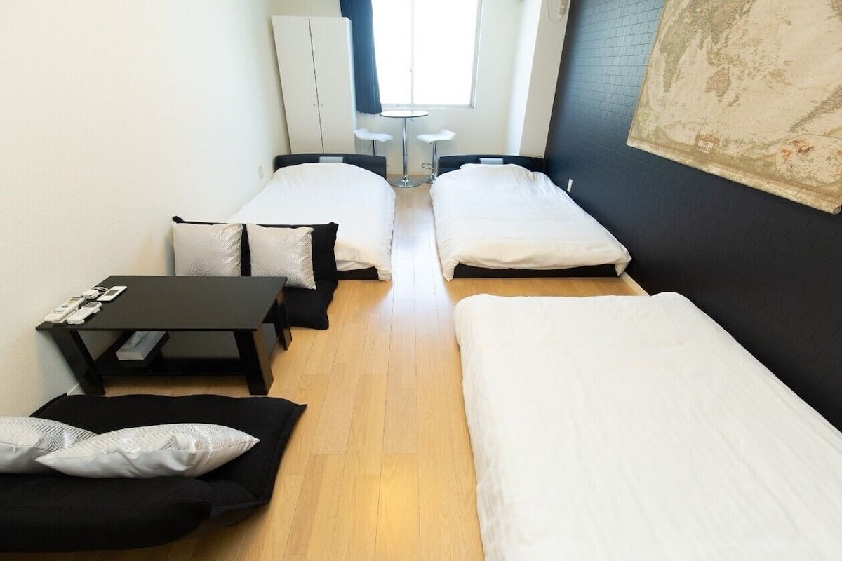 Habitación pequeña con dos camas individuales, una mesita y una silla. Cuenta con una ventana con cortinas, un mapa en la pared y un armario.