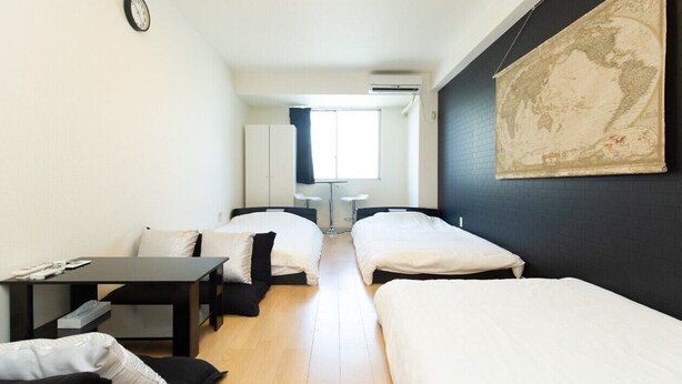 A hotel room with two beds, a desk, a chair, a map on the wall, and a window with curtains. - Guesthouse Daikokucho Ekimae (Osaka)