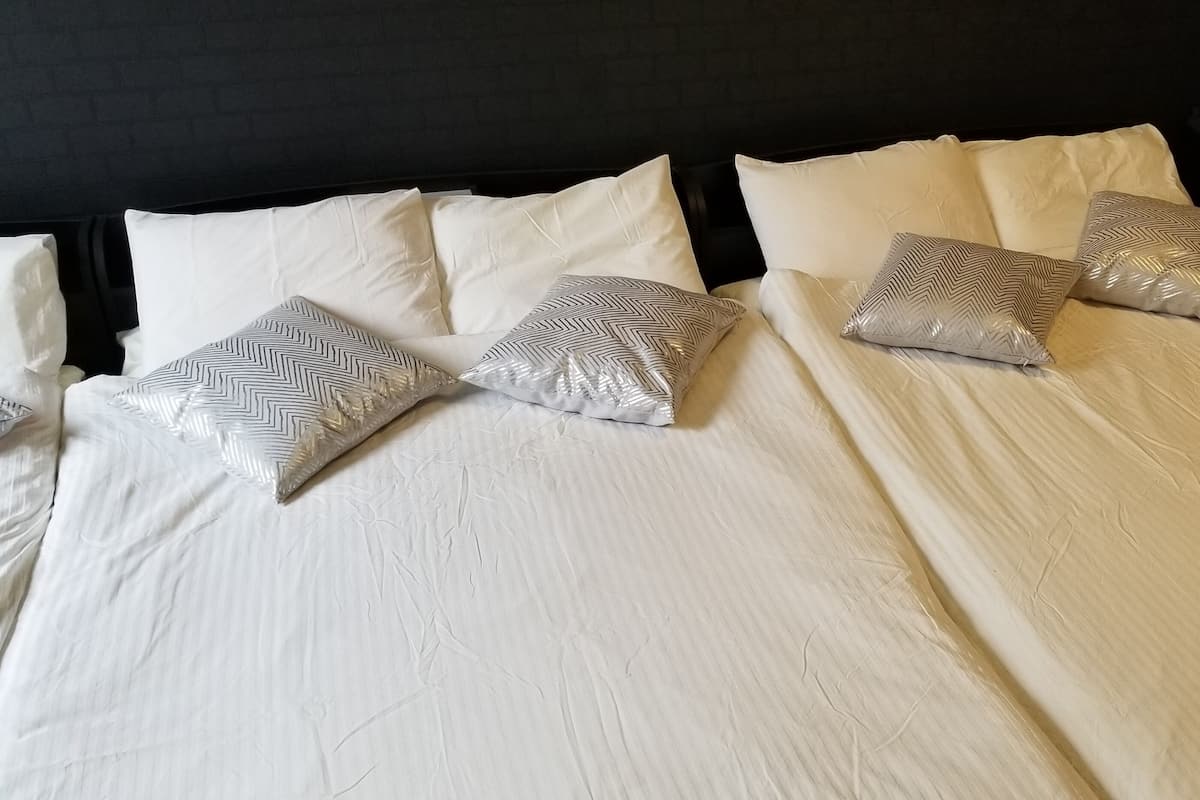 Una cama bien hecha con sábanas blancas y almohadas estampadas.