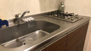 A kitchen with a stainless steel sink, a gas stove, and wooden cabinets. - Local Hakata Apartment (Fukuoka)