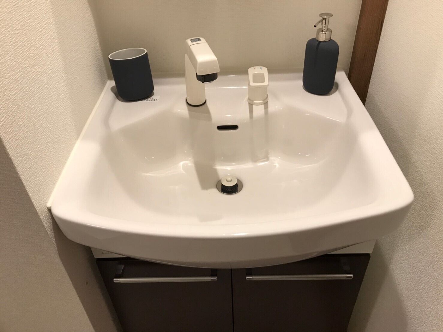 A white bathroom sink with a faucet, a soap dispenser, and a cup.