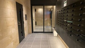 A hallway with a tiled floor, a door on the left, and a row of safes on the right. - Local Hakata Apartment (Fukuoka)