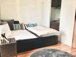 A modern bedroom with a black bed, white bedding, and striped pillows. There is a wooden floor and a gray rug. - Local Hakata Apartment (Fukuoka)
