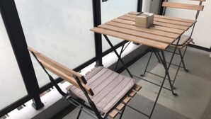 A small, enclosed balcony with a wooden table and two chairs, a small potted plant, and a view through a frosted glass door. - Local Hakata Apartment (Fukuoka)