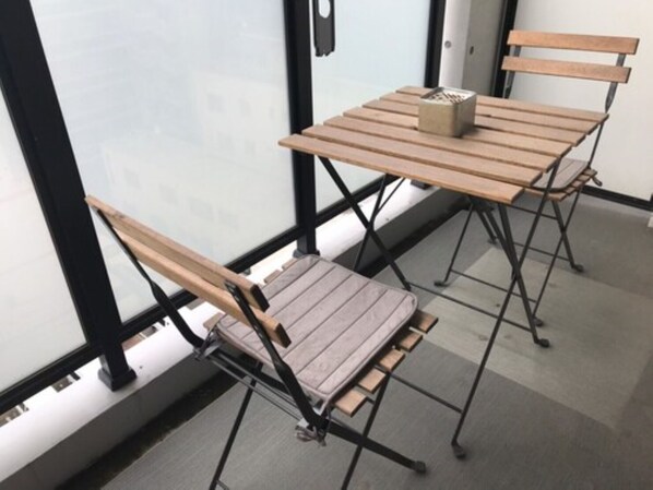 A small, enclosed balcony with a wooden table and two chairs, a small potted plant, and a view through a frosted glass door. - Local Hakata Apartment (Fukuoka)