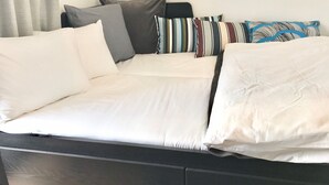 A bed with white bedding and multiple pillows in various colors and patterns. - Local Hakata Apartment (Fukuoka)