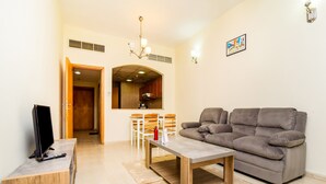 Un soggiorno con un divano grigio, un tavolino in legno, una TV su un mobile basso e una zona pranzo con sedie e tavolo.