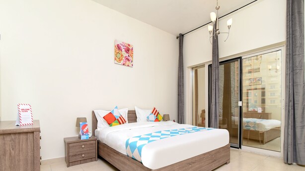 Una camera d'albergo moderna con un letto grande, un comodino in legno, un tavolino da notte con una lampada e vista all'esterno attraverso una porta in vetro.