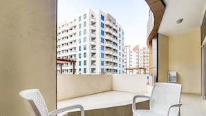 Un balcone con due sedie bianche, un tavolino e vista su edifici alti.