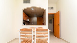 Zona pranzo con tavolo e sedie in legno, cucina visibile tramite un arco, e una porta che conduce in un'altra stanza.