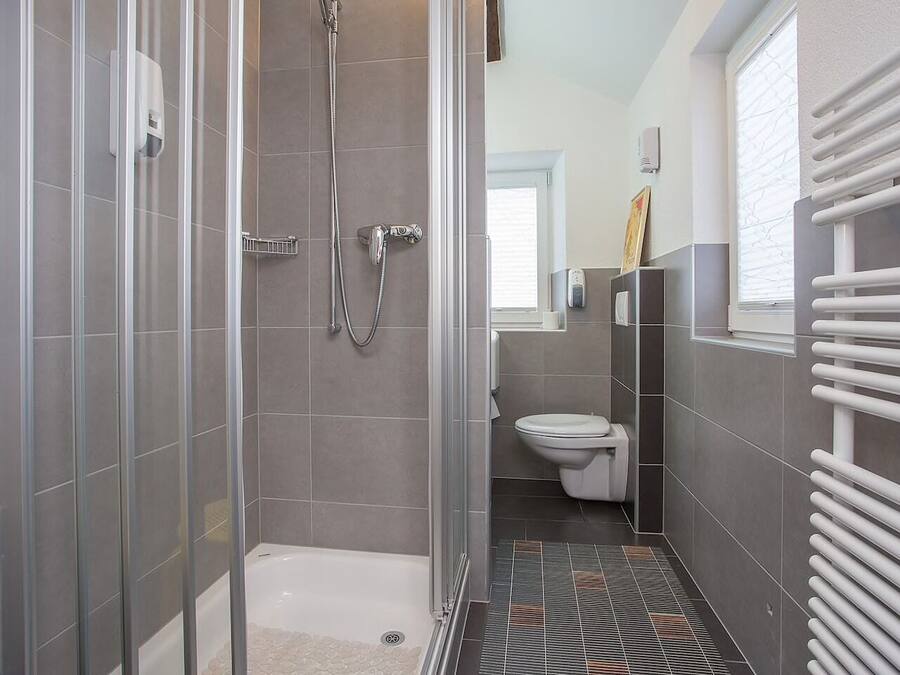 Une salle de bain moderne avec une douche à parois de verre, des toilettes blanches et un sol carrelé.