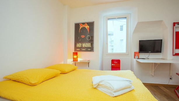 A room with a bed, a TV, a red Intermec device, and a poster on the wall. - Midi Guestrooms (Martigny)