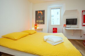 A room with a bed, a TV, a red Intermec device, and a poster on the wall. - Midi Guestrooms (Martigny)