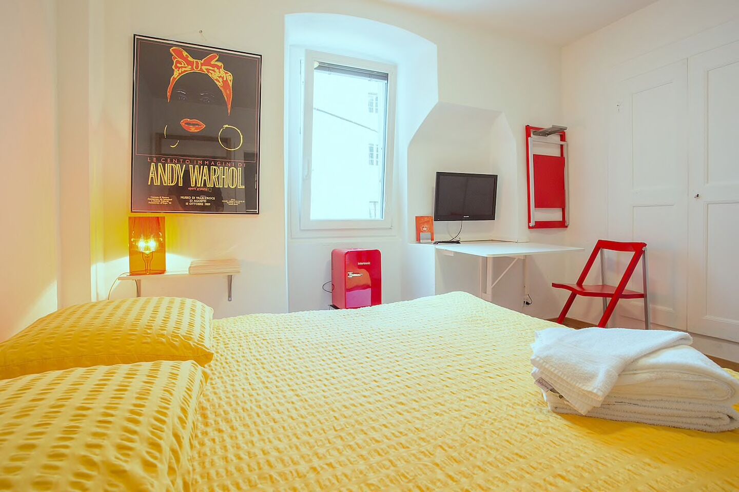 Habitación de hotel con cama, escritorio, silla, televisión y un cartel en la pared.