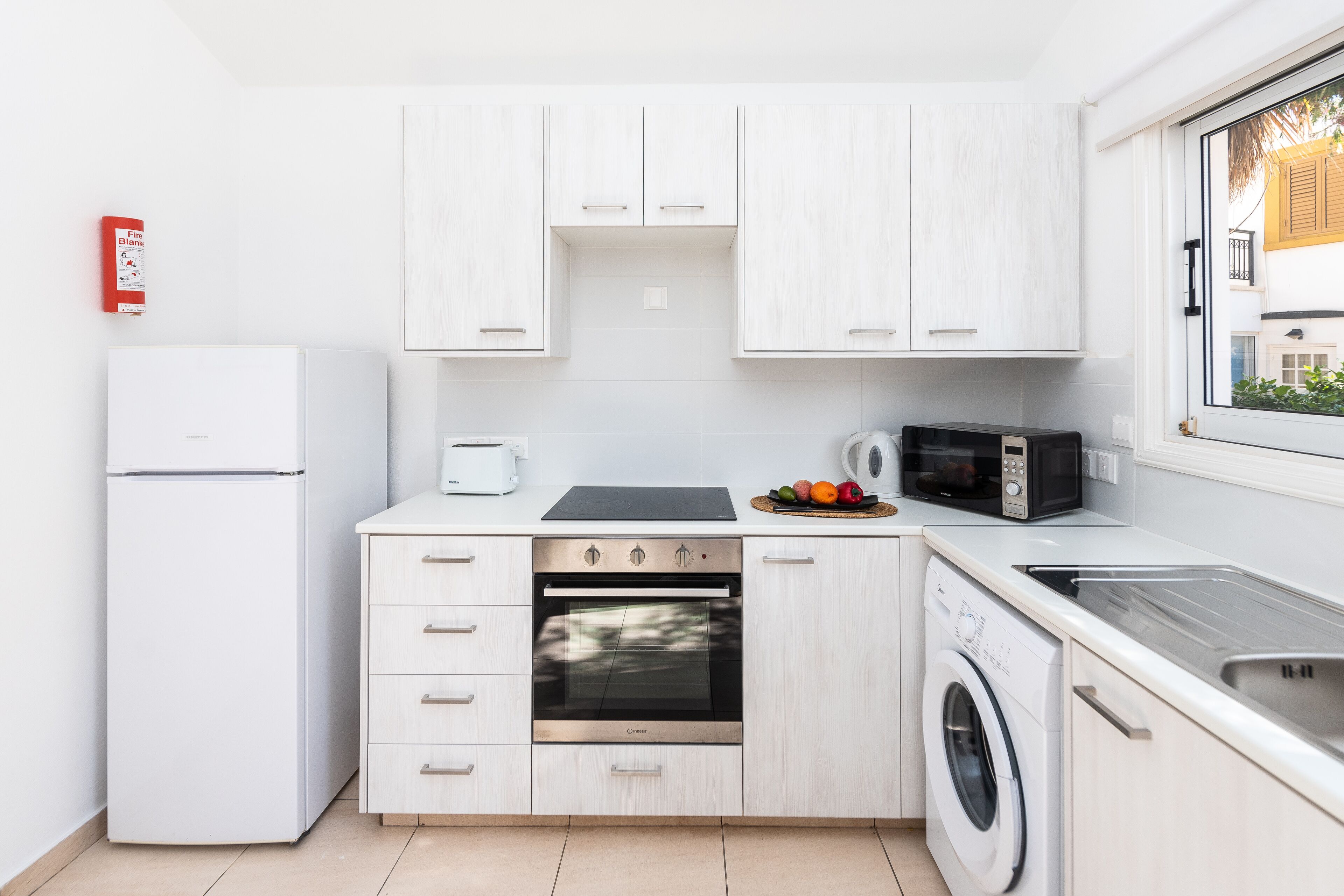 A modern kitchen with white cabinetry, a built-in oven, a microwave, a washing machine, and a refrigerator.