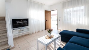 Un soggiorno moderno con una TV a schermo piatto su un mobile bianco, un divano blu, un tavolino da caffè con un vaso di fiori e una scala a sinistra.