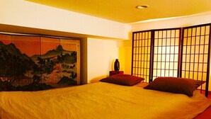 Une chambre avec un grand lit, un tableau accroché au mur et un paravent japonais traditionnel en papier.