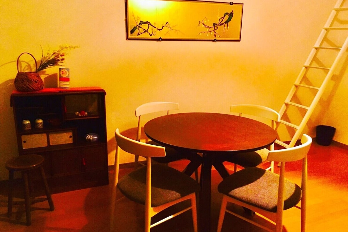 A dining area with a round table and four chairs, a small stool, a bookshelf, and a ladder against the wall.