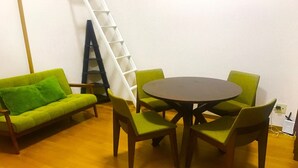 Une pièce avec un canapé vert, une table ronde entourée de chaises et une échelle appuyée contre le mur.